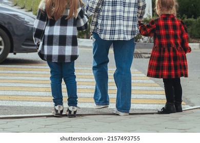 mother took her children by the hands and teaches them to cross the road correctly and safely along the pedestrian crossing where a zebra is drawn on the ground