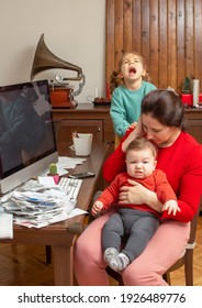 Mother With Two Child At Home. Kids Crying. Childcare And Working Mom. Woman Talk By Phone. Toddler Tantrum. Young Lady Working At Home During Quarantine. Real People. A Lot Of Bills On The Table.