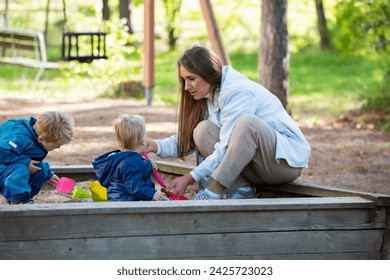 The mother with two children is having a fun time at the playground. Two little boys with their mom playing in the sandbox - Powered by Shutterstock