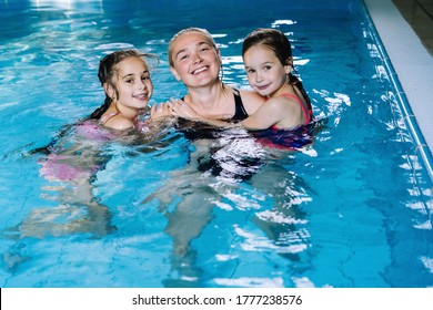 Mother With Two Daughters Having Fun In Indoor Swimming-pool. Girl Is Resting At The Water Park. Swimming School For Small Children. Concept Friendly Family Sport Summer Vacation. Selective Focus.