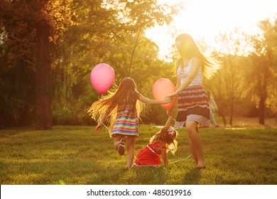 Mother and two daughters holding hands circling. Family time together. Cheerful picnic. Girls with balloons. Soft focus - Powered by Shutterstock