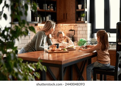 Mother and two daughters share the kitchen table, with mom and the elder sister working on homework together while the younger one joyfully doodles. A delightful morning of togetherness. - Powered by Shutterstock