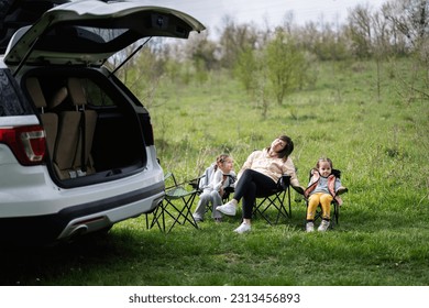 Mother with two daughters sit on chair against car open trunk on picnic. - Powered by Shutterstock