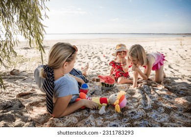 Mother and two daughters are sitting on sand eating the watermelon. Picnic on a beach. Sea travel holiday. Mommy care and love. Happy moments. Strengthening relationships parents and children. Morning - Powered by Shutterstock