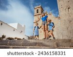 Mother with two kids do sightseeing in Spain Peniscola old town stand in front of church of the Ermitana observe castle walls on sunny day