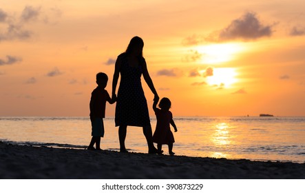 Mother And Two Kids Walking On Beach At Sunset