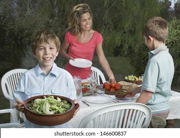 Mother And Two Sons Setting The Dinner Table In Garden