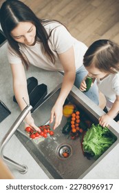 Mother and two-year-old daughter wash vegetables in the kitchen sink. Cooking and health care. View from above. Close-up. - Shutterstock ID 2278096917