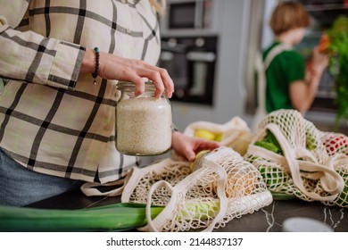 Mother Unpacking Local Food In Zero Waste Packaging From Bag With Help Of Daughter In Kitchen At Home.