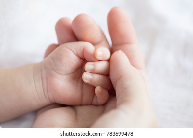 Mother uses her hand to hold her baby's tiny hand to make him feeling her love, warm and secure.