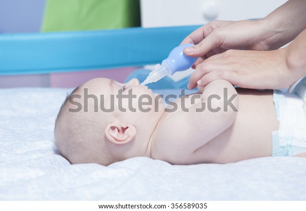 Mother using baby nasal aspirator. She is doing a mucus suction to three months baby boy