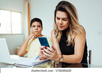 Mother Using Cell Phone Ignoring Her Son While He Is Doing Homework. Concept Of Home Education In Quarantine. Difficulties Of Distance Learning