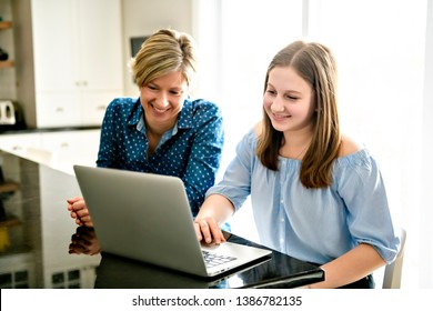 A mother using a laptop in kitchen with teenager