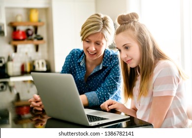 A mother using a laptop in kitchen with teenager