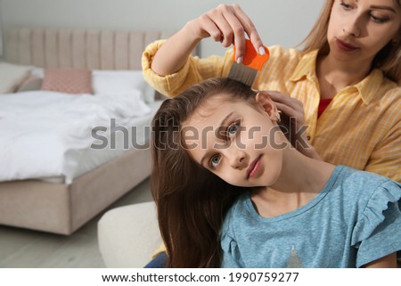 Mother using nit comb on her daughter's hair in bedroom. Anti lice treatment