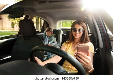 Mother Using Phone While Driving Car With Her Son On Backseat. Child In Danger