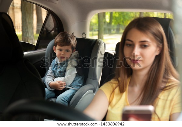 Mother using phone while driving car with her son\
on backseat. Child in\
danger