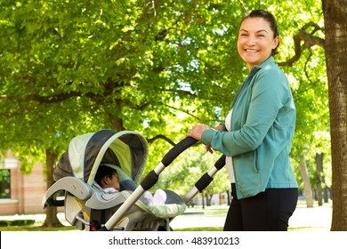 Mother Walking While Pushing A Stroller In The Park.