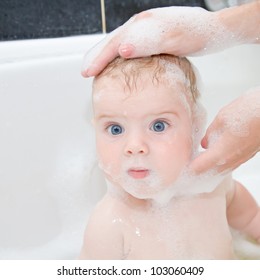 Mother Washing Baby Hair In Bath. Baby With Big Blue Eyes Surprised