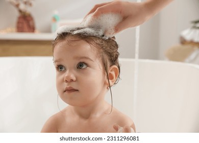Mother washing her little daughter`s hair with shampoo in bathroom, closeup - Shutterstock ID 2311296081