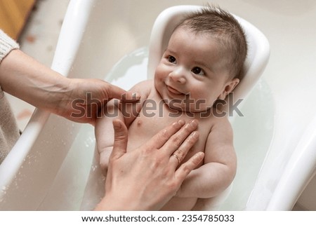 Mother washing her smiling baby in bathtub