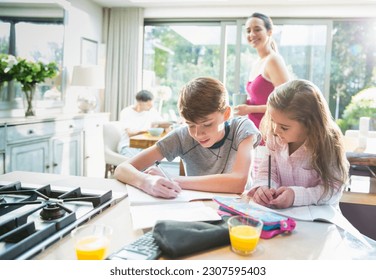 Mother watching brother and sister doing homework at kitchen counter - Powered by Shutterstock