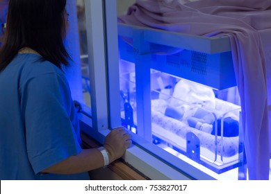 Mother Watching At The Newborn Baby With Hyperbilirubinemia / Neonatal Jaundice Under Blue UV Light For Phototheraphy On Infant Warmer In Neonatal Intensive Care Unit