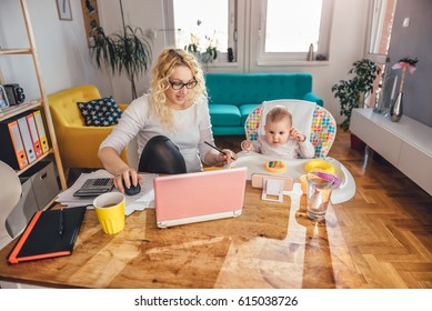 Mother wearing eyeglasses working at home office on laptop and taking care of her baby - Powered by Shutterstock