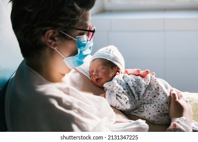 Mother Wearing A Face Mask While Holding Her Newborn Baby In The Hospital Room.