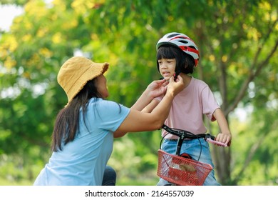 Mother Wearing A Helmet To Her Daughter With Love She Is To Ride A Bike And Exercise In The Park. To Care And For The Safety Of My Daughter It's A Family Outdoor Activity. Daughter Smiling Happiness.