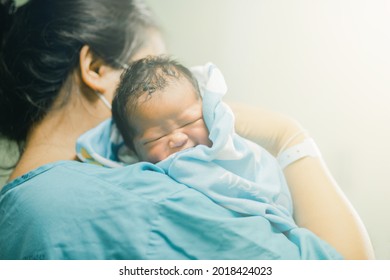 A mother wearing a mask is holding a newborn woman in the hospital.
