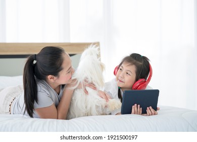 A mother whose daughter is using The tablet is in a bed with white-haired maltese dogs.
