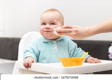 Mother Wipes Baby's Mouth With Napkin After Feeding Her Baby Son With Food At Home