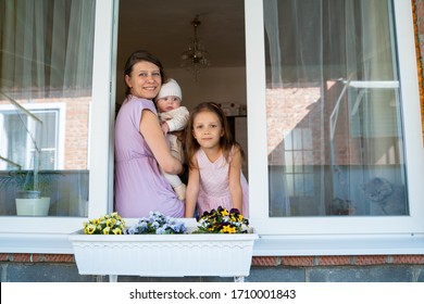 Mother woman with a newborn baby and girl child preschooler looking out the window from her home while being isolated from coronavirus - Shutterstock ID 1710001843