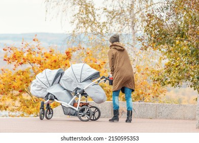 Mother Woman Walks With Twin Baby Stroller Or Pushchair In Autumn Park