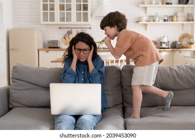 Mother Working From Home Cover Ears With Hands To Protect From Loud Noises From Hyperactive Preschool Child Try To Focus On Laptop Computer On Covid-19 Lockdown School Closed And Remote Work Lifestyle