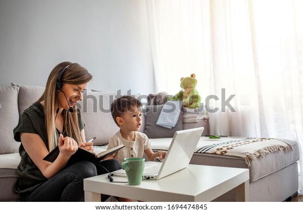 Mother working from\
home with young children in quarantine isolation Covid-19. Mother\
working from home with kid. Quarantine and closed school during\
coronavirus outbreak.
