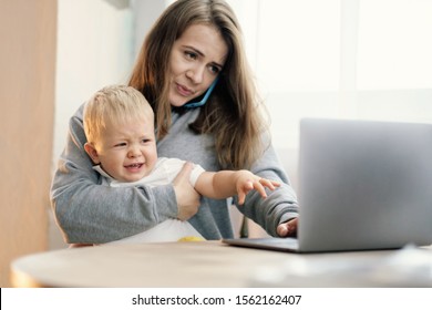 mother works at computer with child, baby is crying, hard work mom with baby