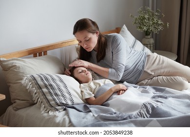 Mother worried son health check hot forehead lying on bed pillow. Unhappy preschooler feeling head pain ache virus disease at home. Female babysitter taking care male kid. Child boy have fever symptom