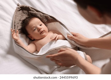 Mother wrapping her cute little baby with hooded towel after bathing on bed, above view - Powered by Shutterstock