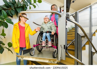 Mother with a young child living with cerebral palsy using electric wheelchair lift to access public building. Special lifting platform for wheelchair users. Disability stairs lift facility.