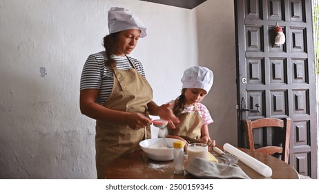 Mother and young daughter bonding while baking in the kitchen. Both are wearing aprons and chef hats, enjoying quality family time. - Powered by Shutterstock