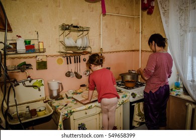 Mother And Young Daughter Preparing Food In The Kitchen, Daughter Standing On A Stool And Helps Mom