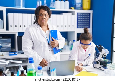 Mother And Young Daughter Working At Scientist Laboratory Scared And Amazed With Open Mouth For Surprise, Disbelief Face 