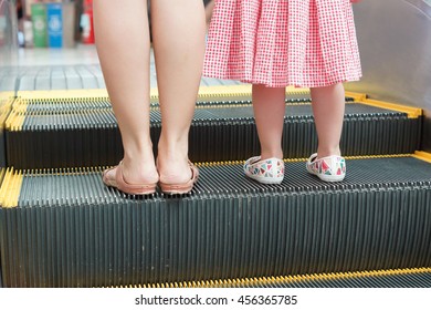 Mother and a young female kid on a moving escalator / Do not let a child go alone on an escalator concept