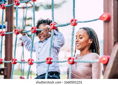 Mother And Young Kid Son African Black Race Play Together At The Playground Park Having Fun And Enjoying The Outdoor Leisure Activity - Family With Dreadlocks Hair Ethnic Style