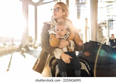 Motherat travelling with his infant baby boy child, walking, pushing baby stroller and luggage cart in front of airport terminal station - Shutterstock ID 2253426095