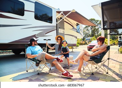 Mother,father,son And Grandmother Sitting Near Camping Trailer,smiling.Woman,men,kid Relaxing On Chairs Near Car.Family Spending Time Together On Vacation In Modern Rv Park