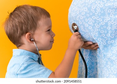 Motherhood, hot summer - croped portrait pregnant mother unrecognizable woman blue dress little boy son sibling treat pregnant mom role play stethoscope unborn brother mom tummy on yellow background