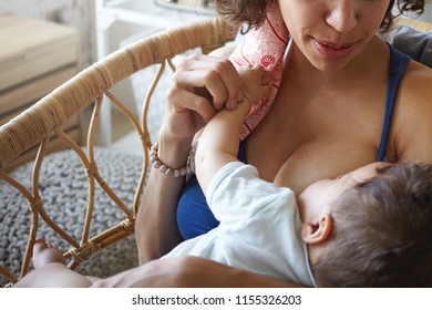 Motherhood and lactation concept. Ideal nutrition for infants. Cute baby sucking breast milk rich in vitamins, fats and protein before sleep. Unrecognizable young mother breastfeeding toddler